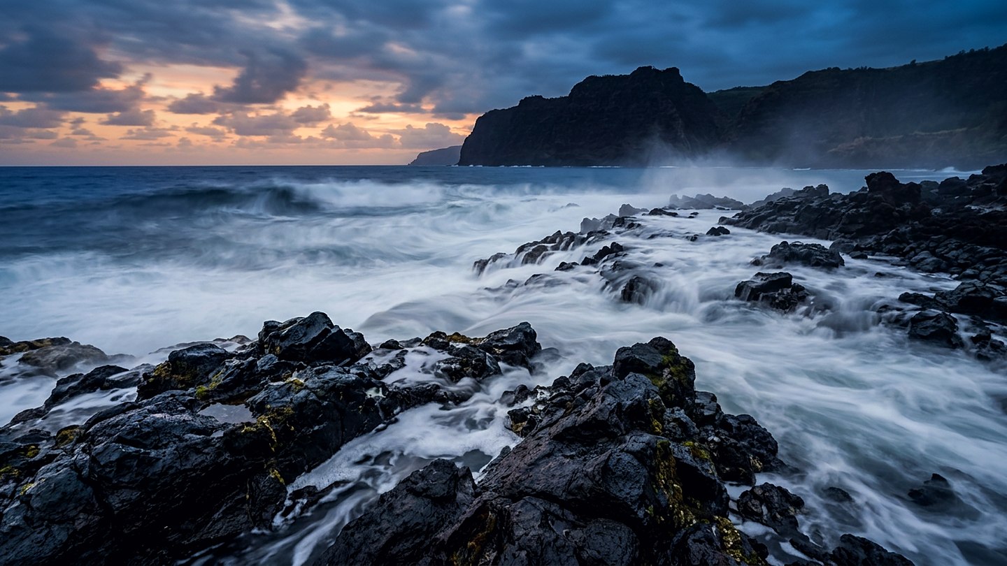 Long exposure of ocean swell moving over dark rock at dusk with soft blue light on the water